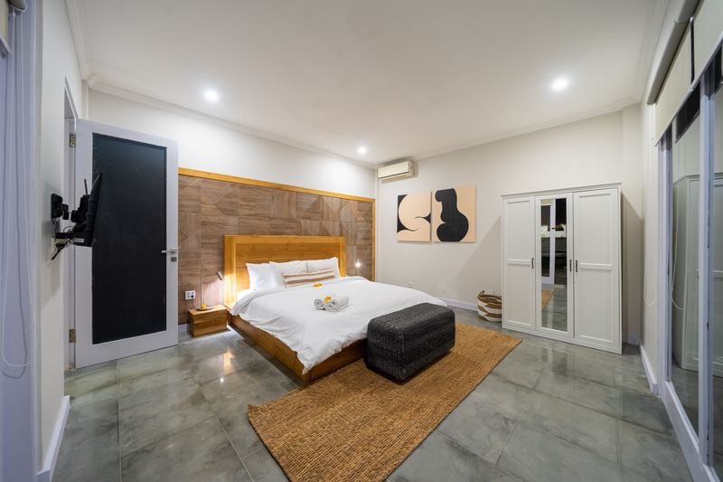 Super king bedroom with timber panelled headboard, smart TV and polished concrete floor