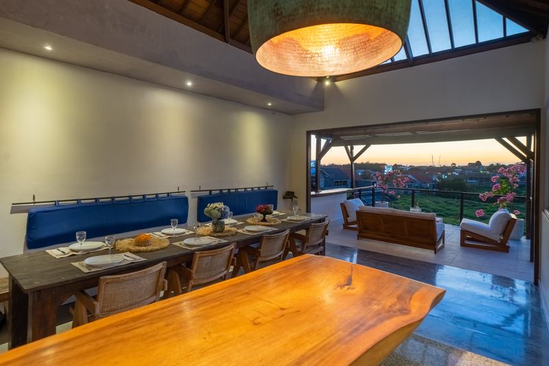 Long timber dining table seating eight, opening onto the view over Berawa